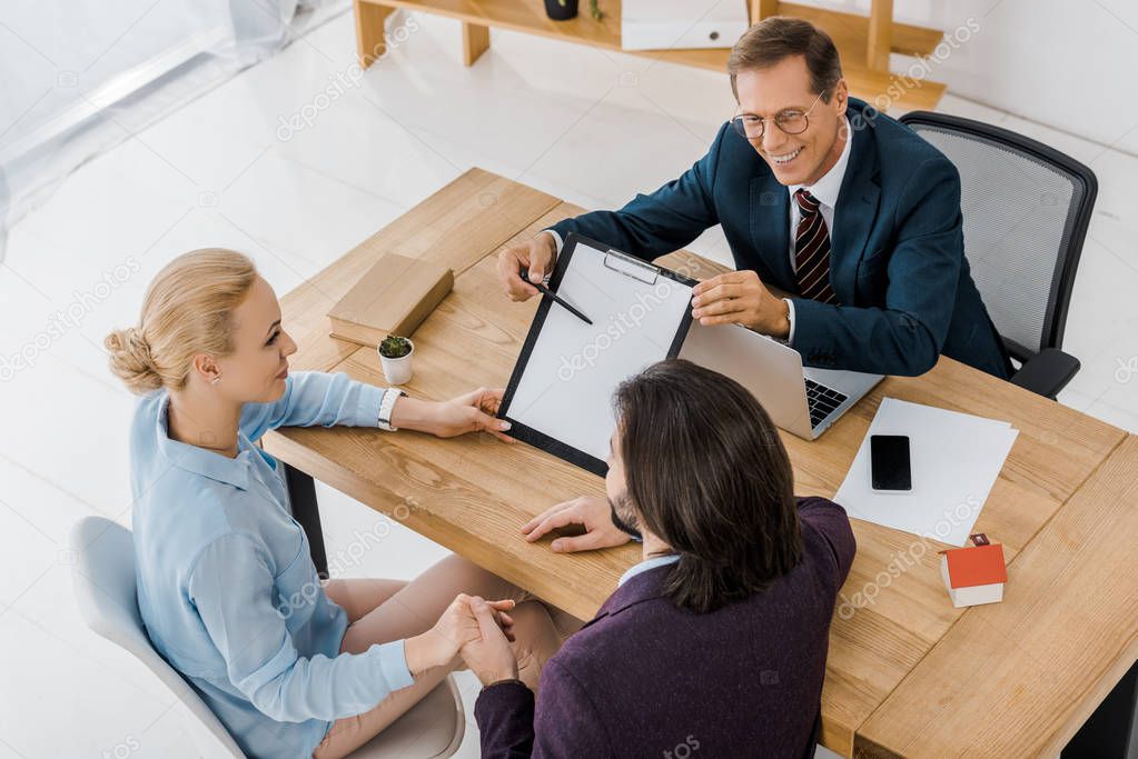 adult insurance agent in glasses showing contract to young couple in office