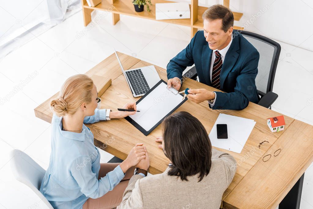 businessman holding keys while couple holding hands and signing contract on clipboard