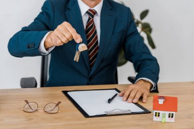 insurance agent holding keys with house model and glasses on table clipart