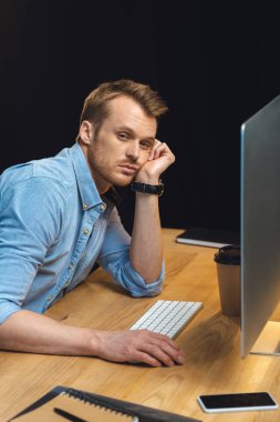 masada akıllı telefon ve bilgisayar ile geç gece boyunca ofiste otururken kameraya bakarak yorgun işadamı yüksek açılı görünüş 