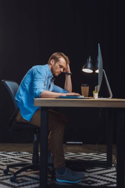 Masa lambası, kahve fincanı ve ofiste bilgisayar ile masada Uyuyan Genç overworked işadamı 