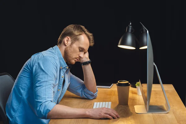 side view of businessman sleeping at table with computer and paper coffee cup during night time in office