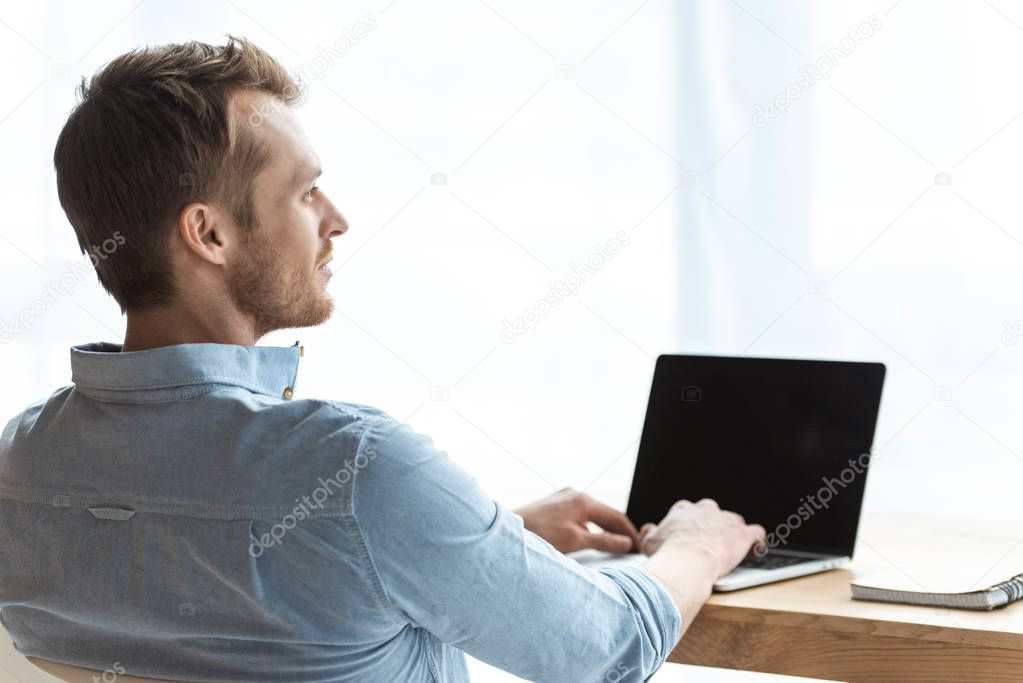 rear view of young businessman working on laptop with blank screen at table in office 