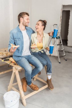 birlikte oturan ve birbirlerine tamirata sırasında gülümseyen pizza ve kağıt bardak ile mutlu genç çift