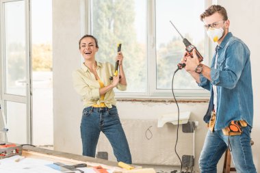 happy young couple holding tools and having fun in new apartment clipart