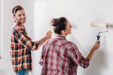 happy young couple in checkered shirts painting wall in new apartment clipart