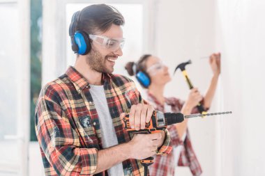 happy young man using electric drill during house repairment clipart