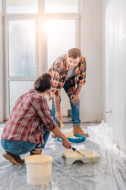 young couple in checkered shirts holding paint rollers and painting wall clipart