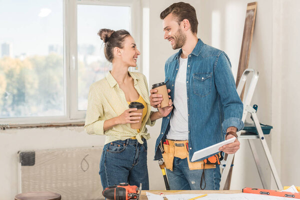 happy young couple holding coffee to go and digital tablet during renovation