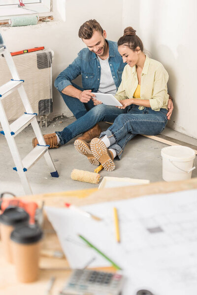высокий угол обзора улыбающейся молодой пары с помощью цифрового планшета во время ремонта дома
