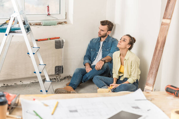 thoughtful young couple sitting in floor and looking away during house repair