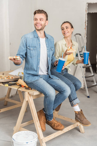 smiling young couple holding pizza and paper cups during house repair 