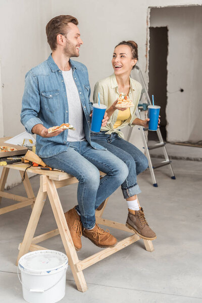 happy young couple holding pizza and paper cups during house repair 