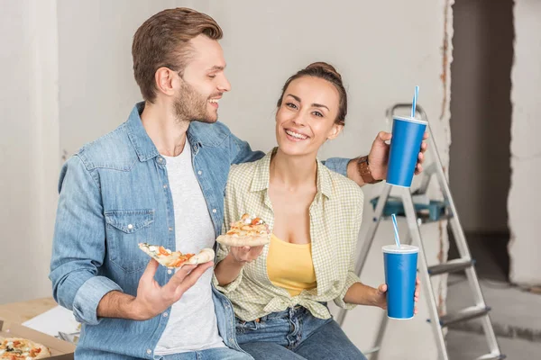 車検中にストローとピザのスライスを飲むと紙コップを抱いた若い夫婦の笑顔 — ストック写真