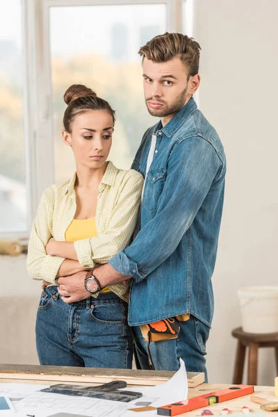 Upset Young Man Hugging Disappointed Girlfriend Looking Camera House Repair — Stock Photo, Image