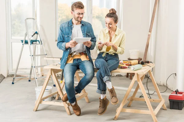 Feliz Pareja Joven Usando Dispositivos Digitales Mientras Hacen Reparación Juntos —  Fotos de Stock