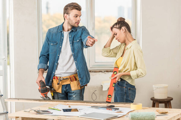 emotional young couple holding tools and quarreling during renovation