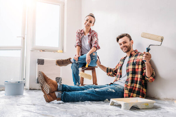happy young couple holding paint rollers and smiling at camera during renovation
