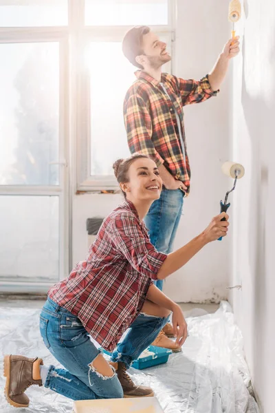 幸福的年轻夫妇在新公寓用油漆辊粉刷墙壁 — 图库照片