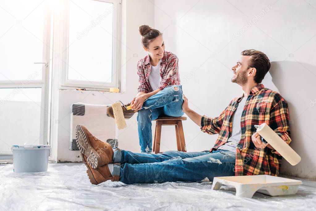 happy young couple holding paint rollers and smiling each other while having break during repairment