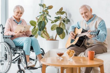 Tekerlekli sandalyede oturan ve komuta sizde akustik gitar çalmak kitabı okuma kadın kıdemli