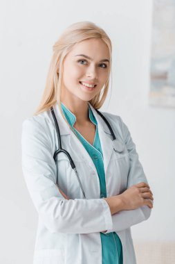 smiling young female doctor with stethoscope standing with arms crossed in clinic  clipart