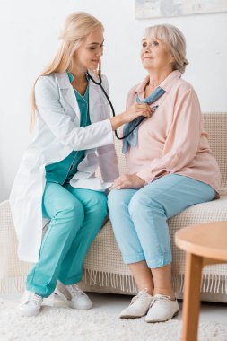 genç gülümseyen kadın doktor stetoskop üst düzey kadın kanepe ile incelenmesi