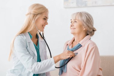 young smiling female doctor examining with stethoscope senior woman clipart