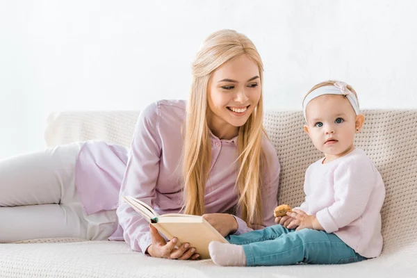 Joven Sonriente Madre Leyendo Libro Pequeña Hija Mientras Niño Sosteniendo — Foto de Stock