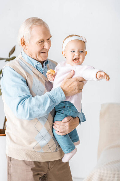 senior smiling grandfather holding toddler granddaughter with cookie