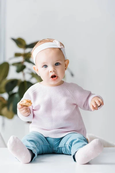 Lindo Niño Sentado Mesa Blanca Sosteniendo Galleta —  Fotos de Stock