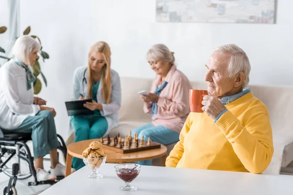 Senior Man Drinking Tea While Doctor Examining Senior Women — Stock Photo, Image