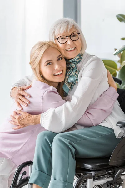 Joven Alegre Mujer Abrazando Senior Mujer Silla Ruedas — Foto de Stock