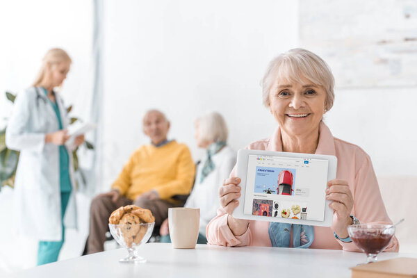 senior woman showing ebay app on digital tablet screen at nursing home