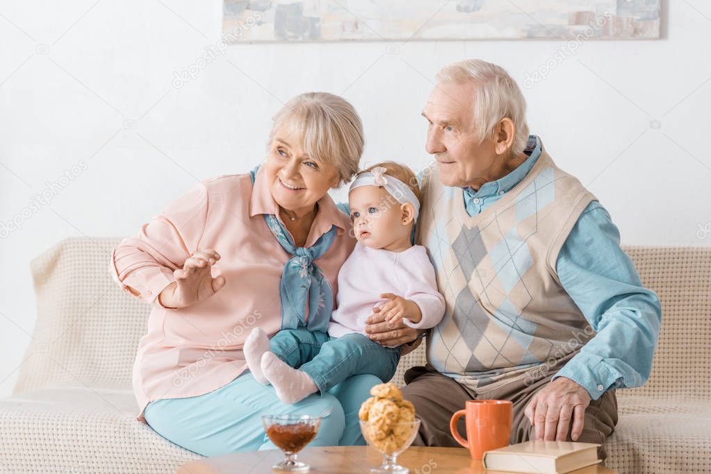 adorable grandparents sitting on sofa with toddler granddaughter
