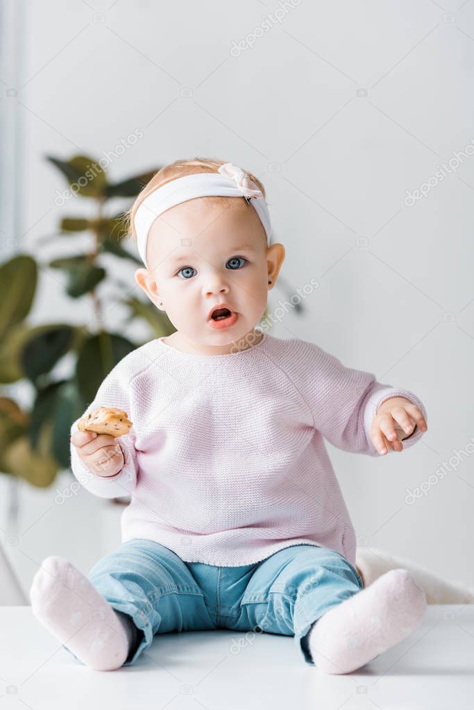 cute toddler sitting on white table and holding biscuit