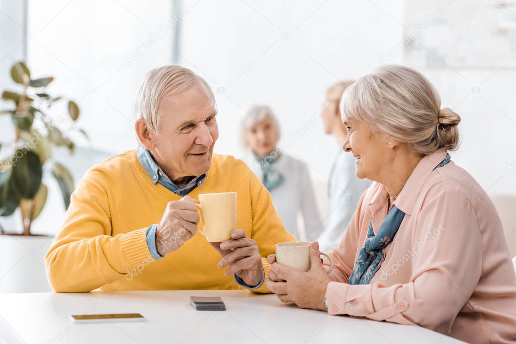 smiling senior man and woman drinking tea at table in clinic