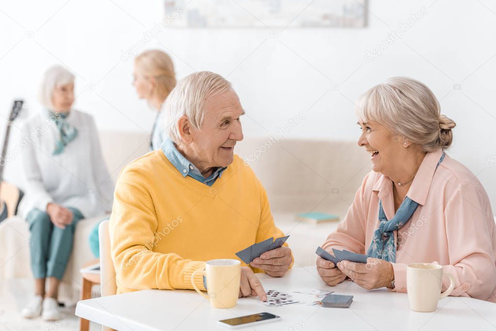 happy smiling senior couple playing cards at table at nursing home