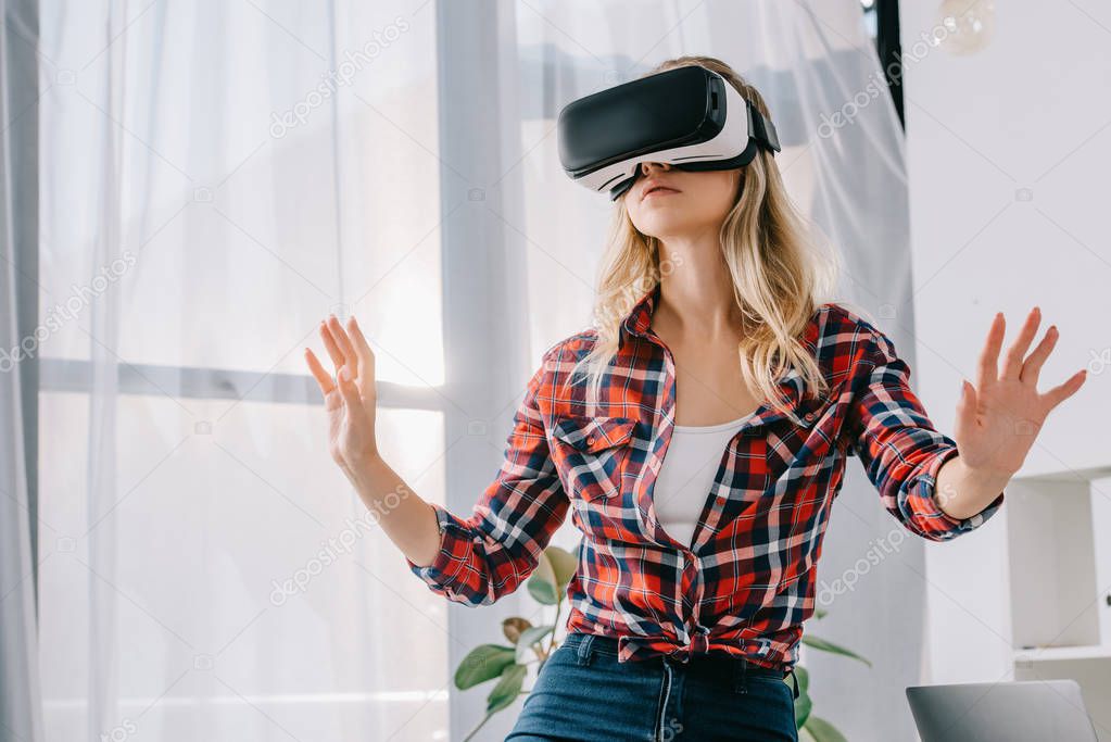 young woman in virtual reality headset gesturing in room
