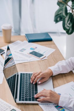 partial view of businesswoman working on laptop with blank screen at workplace in office clipart