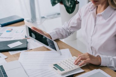 partial view of businesswoman with tablet making calculations at workplace with papers clipart