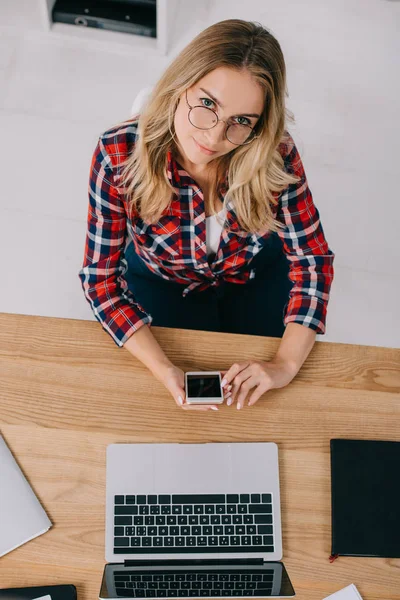 Overhead View Woman Smartphone Looking Camera While Sitting Tabletop Laptop — Free Stock Photo