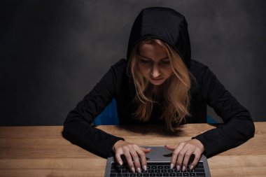 kadın hacker ahşap masa üstü dizüstü kullanarak siyah hoodie'odaklı