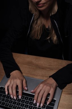 siyah hoodie ahşap masa üstü dizüstü kullanarak atış kadın hacker kırpılmış