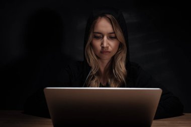 kadın hacker ahşap masa üstü dizüstü kullanarak siyah hoodie'portresi