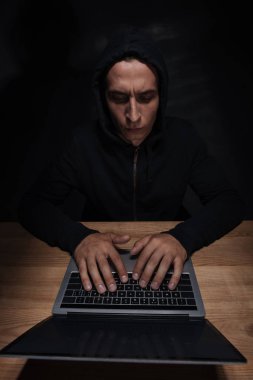 focused hacker in black hoodie using laptop at wooden tabletop, cuber security concept clipart