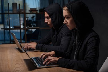 bilgisayar korsanları siyah hoodies ahşap masa üstü, siber güvenlik kavramı dizüstü bilgisayarlar kullanarak yan görünüm
