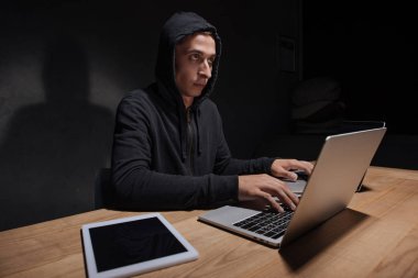 hacker'siyah hoodie tablet karanlık odada, siber güvenlik kavramı ile masaüstü, dizüstü bilgisayarlar kullanarak