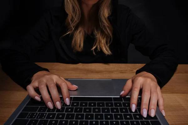 partial view of female hacker using digital laptop at wooden tabletop