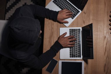 hacker'siyah hoodie tablet ve smartphone, siber güvenlik kavramı ile masaüstü, dizüstü bilgisayarlar kullanarak havai görünümü